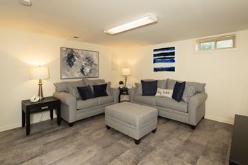 A living room with two grey couches and a grey ottoman.